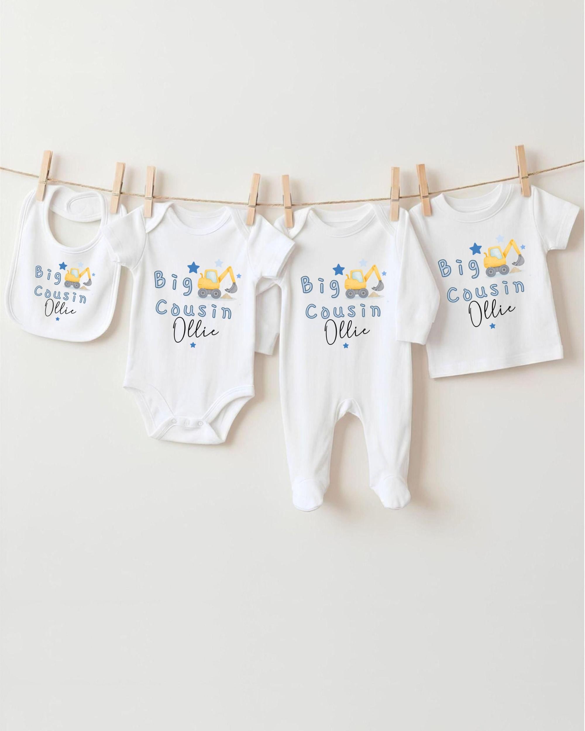 A row of four white baby clothes with blue and yellow construction-themed designs hanging on a clothesline.