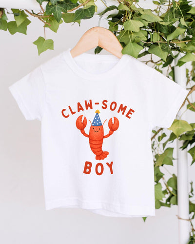 A white t-shirt with a lobster wearing a party hat and the text "CLAW SOME BOY" printed on it.