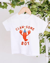 A white t-shirt with a lobster wearing a party hat and the text "CLAW SOME BOY" printed on it.