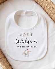 A white baby bib with the name "Baby Wilson" and the date "Due March 2027" printed on it, along with an illustration of a baby elephant.
