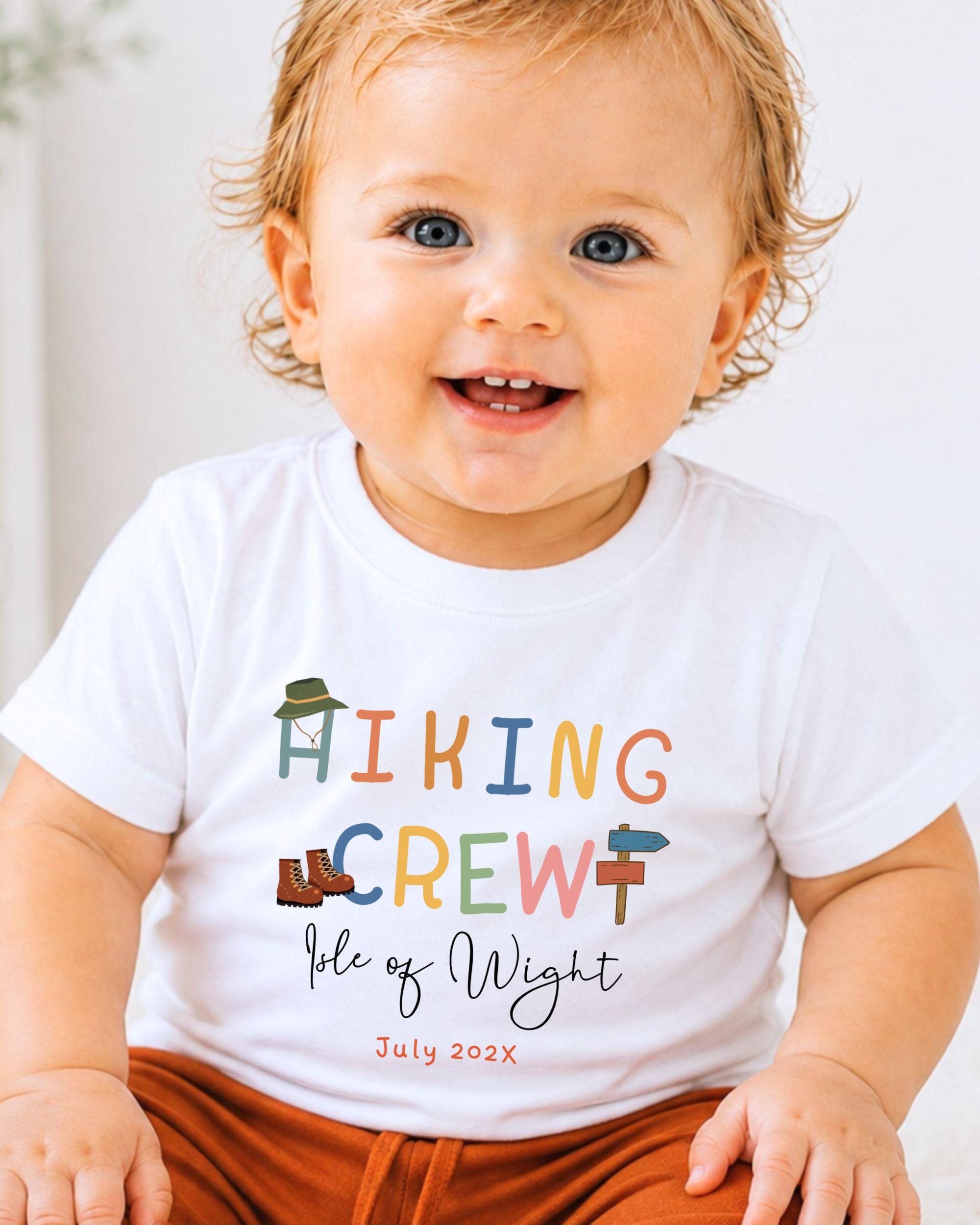 A smiling baby wearing a white t-shirt with colorful text and graphics.