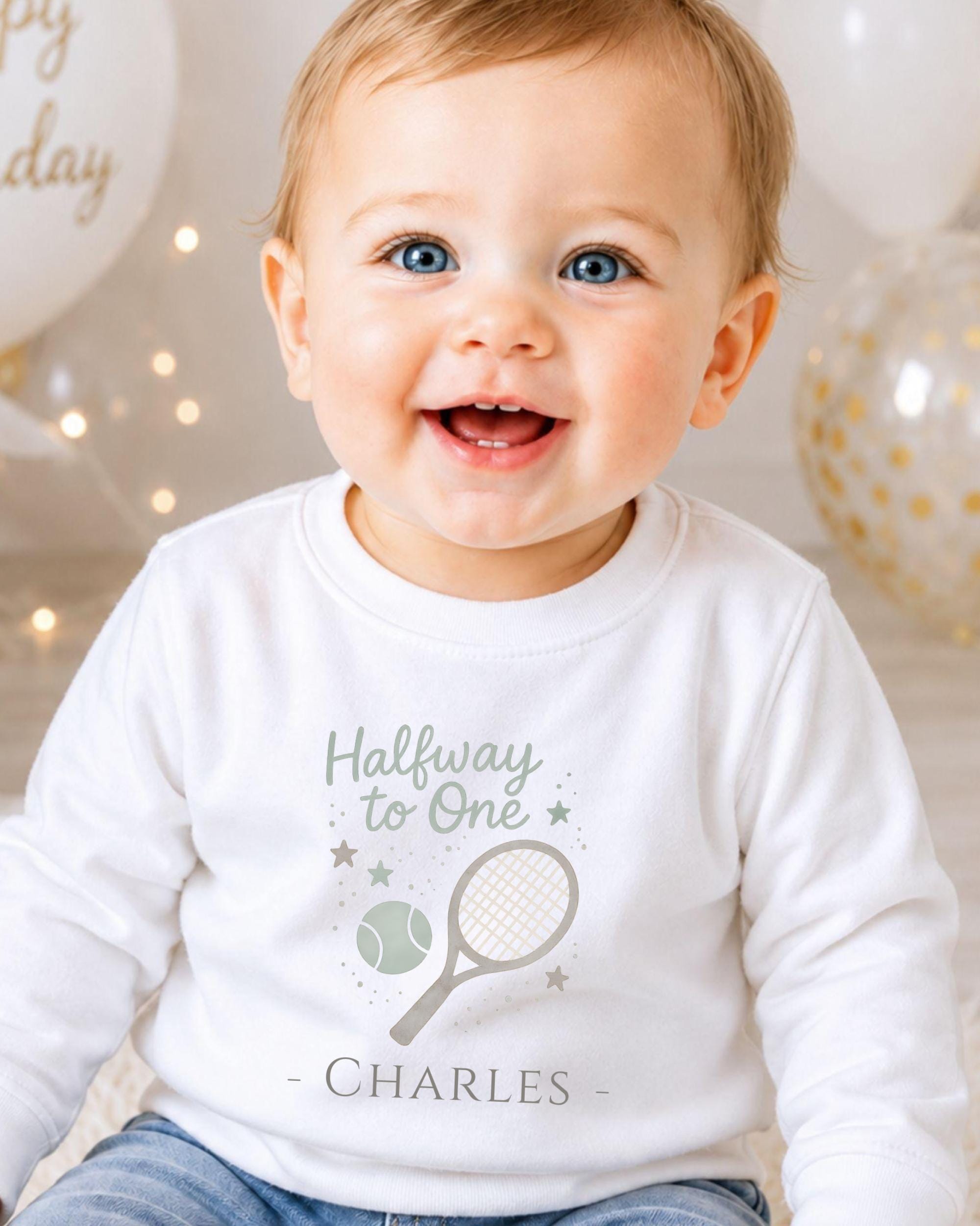 A smiling baby boy wearing a white shirt with a tennis racket and the text "Halfway to One" and "Charles" printed on it.