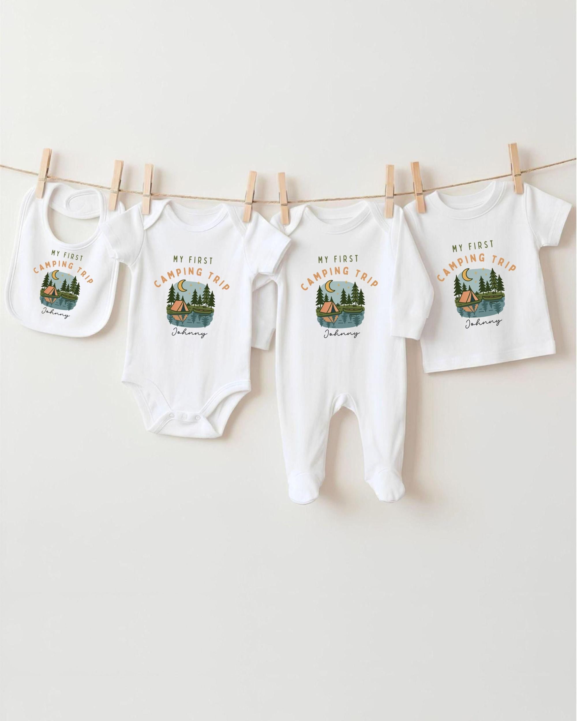 A collection of four white baby clothes, including onesies and bibs, hanging on a clothesline.