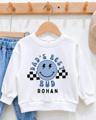A white sweatshirt with a graphic design and text printed on it, hanging on a wooden hanger.