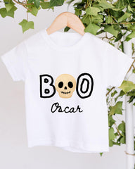 A white t-shirt with a skull design and the text "BOO Oscar" printed on it, hanging on a wooden hanger.