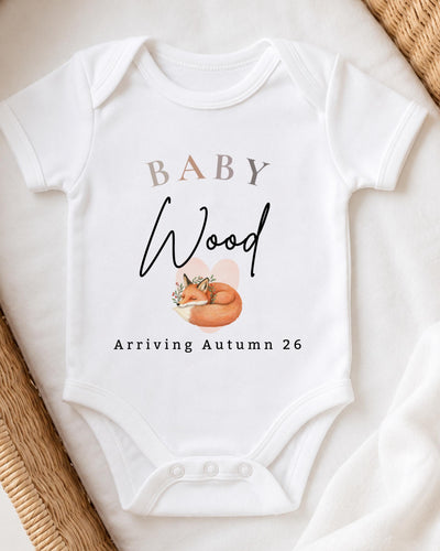Personalisable white Baby Vest with beige 'BABY', black script 'Wood', a sleeping orange fox and 'Arriving Autumn 26' lettering.