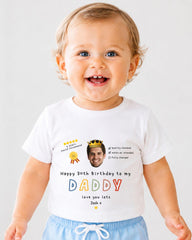 A smiling baby boy wearing a white t-shirt with a personalized message and a crown graphic.
