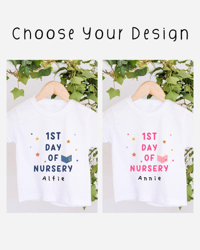 two white t-shirts hanging on a wooden hanger, each with a different design and text. The t-shirts are labeled "1st Day of Nursery" and "1st Day of Nursery" with the names "Alfie" and "Annie" printed on them. The t-shirts are set against a backdrop of greenery, creating a pleasant and natural atmosphere.