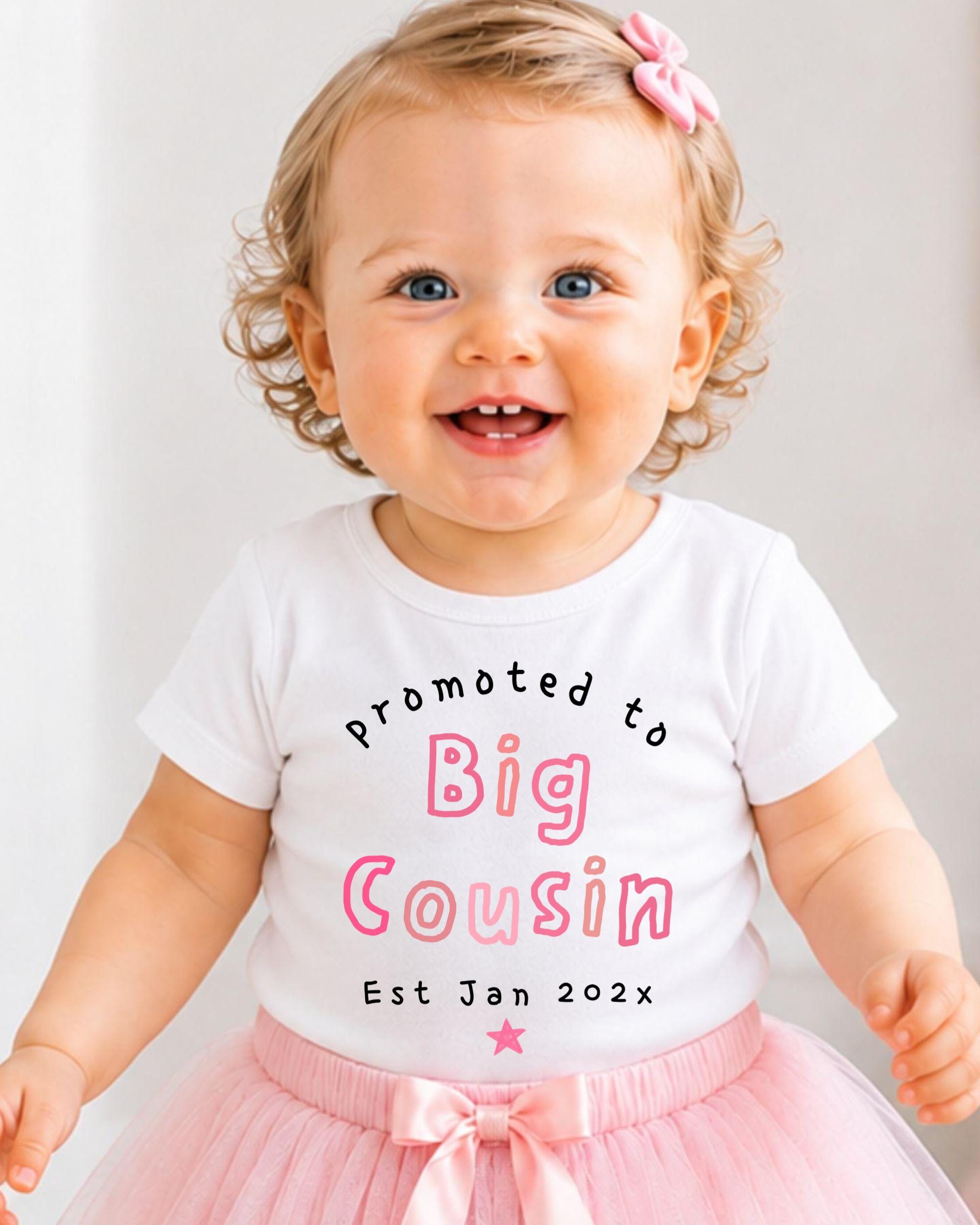 A smiling baby girl wearing a white t-shirt with text and a pink tutu skirt.