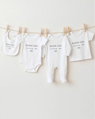 A collection of white baby clothes, including onesies and pajamas, hanging on a clothesline.