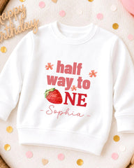 A white sweatshirt with a personalized text and a strawberry graphic printed on it.