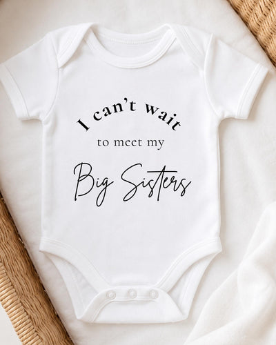 A white baby bodysuit with the text "I can't wait to meet my Big Sisters" printed on it.