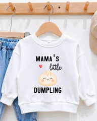 A white sweatshirt with a printed design on it, hanging on a wooden hanger. The design features a smiling cartoon character and the text "Mama's little DUMPLING".