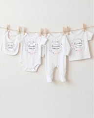 A row of four white baby clothes with floral designs, hanging on a clothesline.
