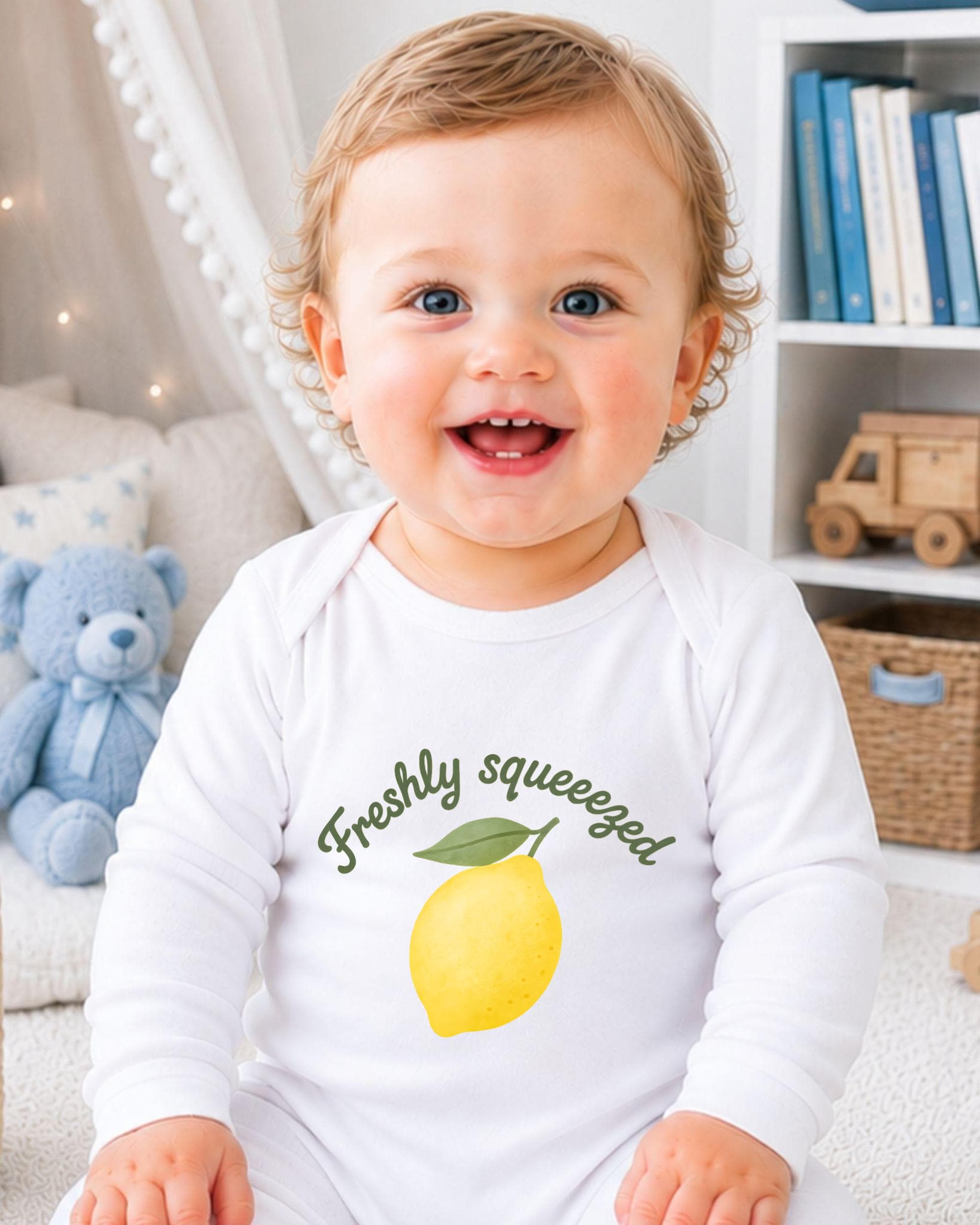 A smiling baby wearing a white onesie with a lemon graphic and the text "Freshly squeezed" is sitting in a room with a blue teddy bear and bookshelf in the background.