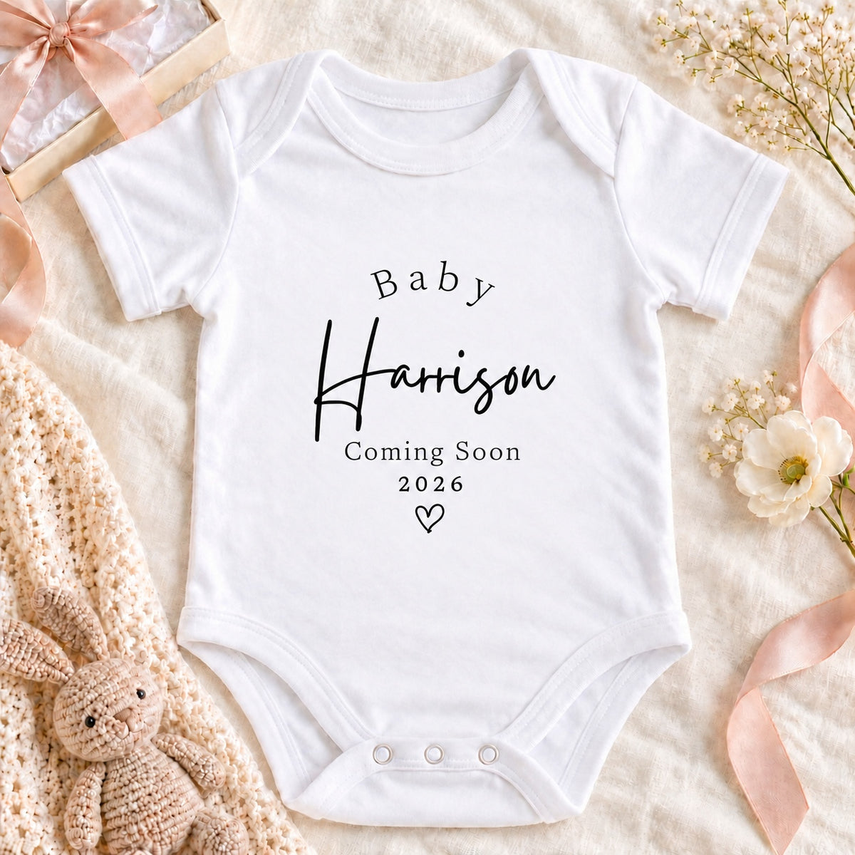 Square pregnancy announcement image of a white Baby Harrison Coming Soon 2026 Baby Vest on beige linen with a cream gift box, ribbon and eucalyptus.