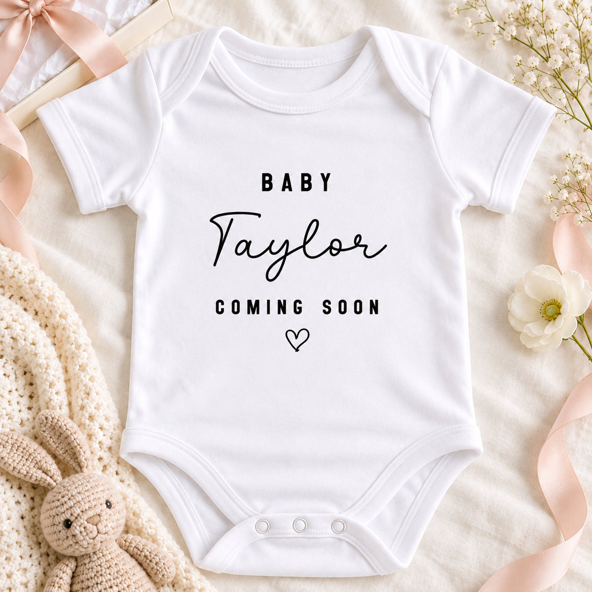 Personalised Baby Taylor Coming Soon pregnancy announcement Baby Vest with cream booties, ivory envelope and eucalyptus on a beige flat lay