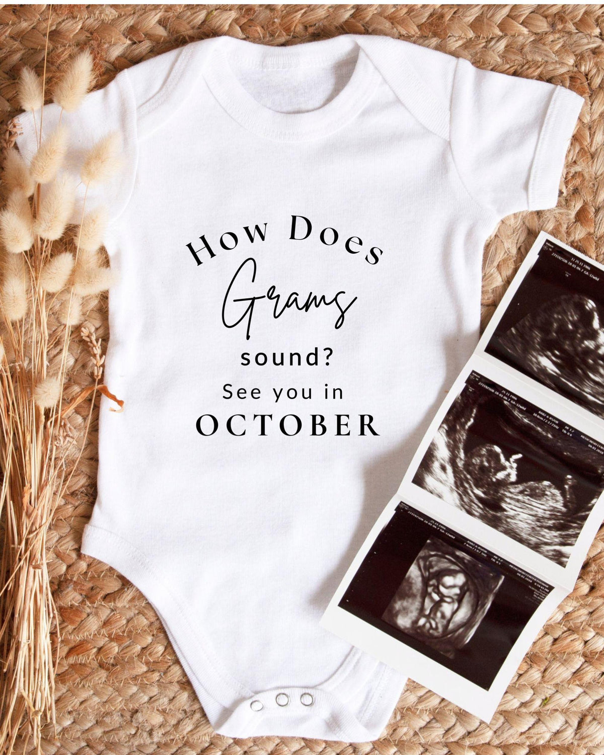 A white baby onesie with text printed on it, placed next to a set of three black and white baby ultrasound images.