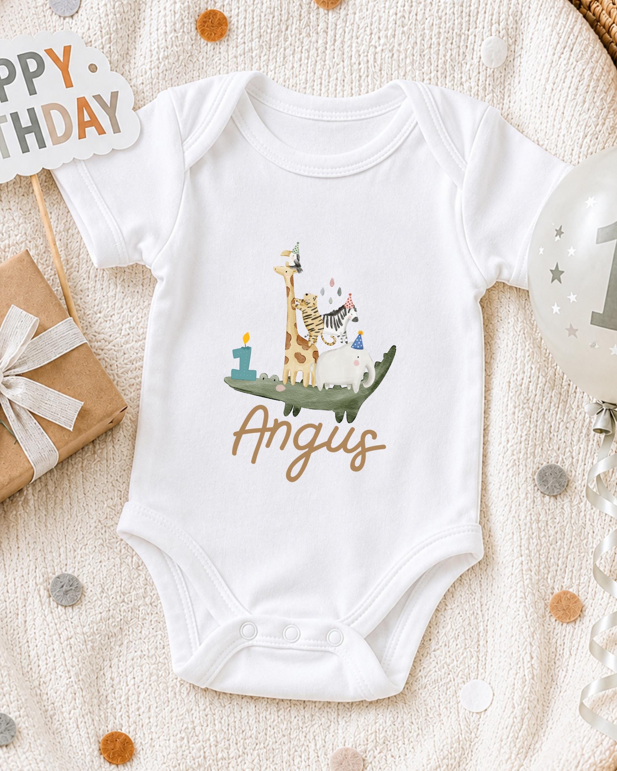 A white onesie with a giraffe and a birthday cake printed on it, along with a "Happy Birthday" sign and a birthday balloon.