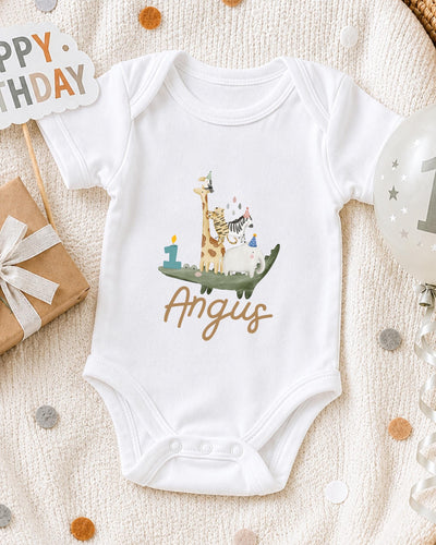 A white bodysuit with a giraffe and a birthday cake printed on it, along with a "Happy Birthday" sign and a birthday balloon.