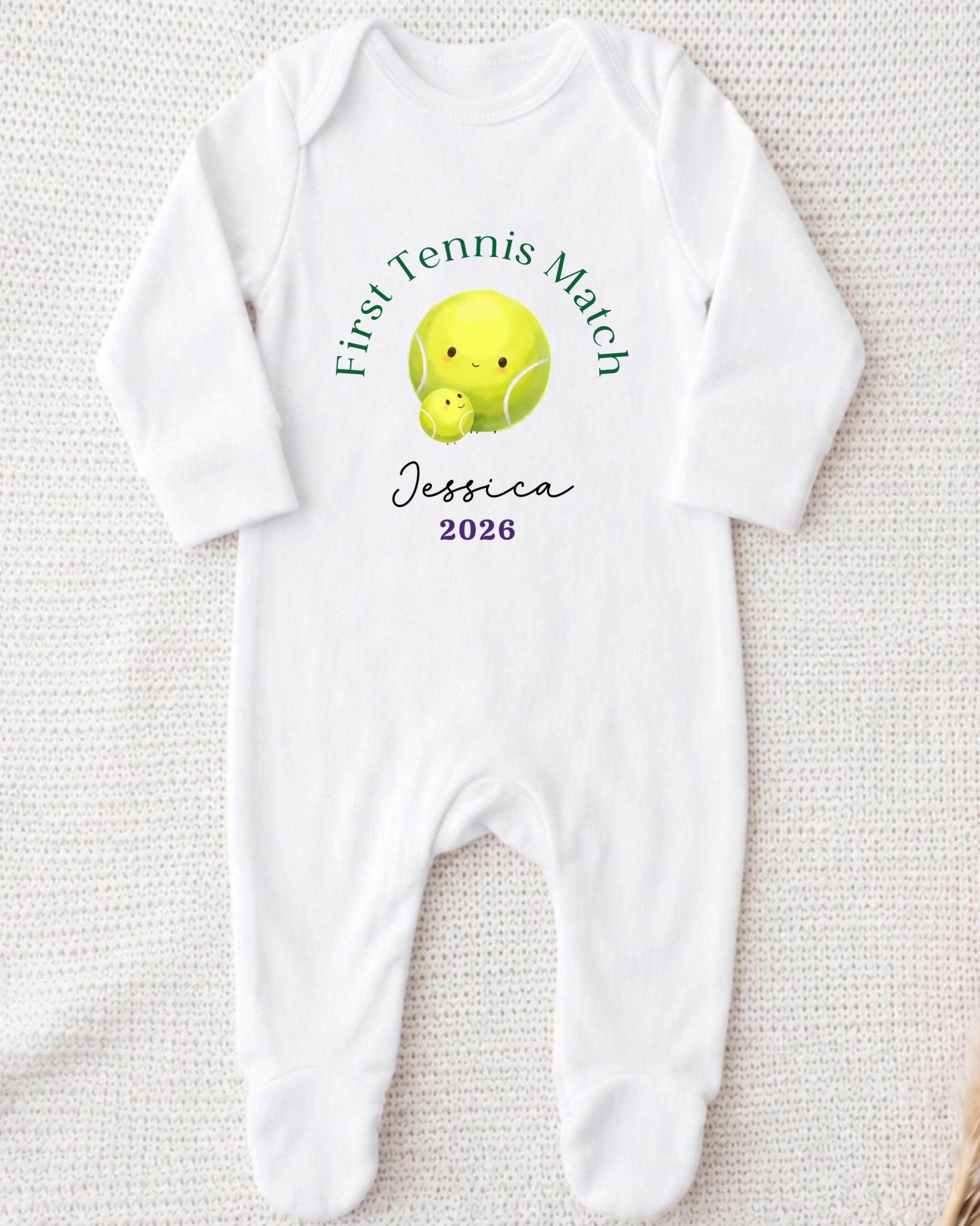 A white onesie with a tennis ball design and text printed on it.