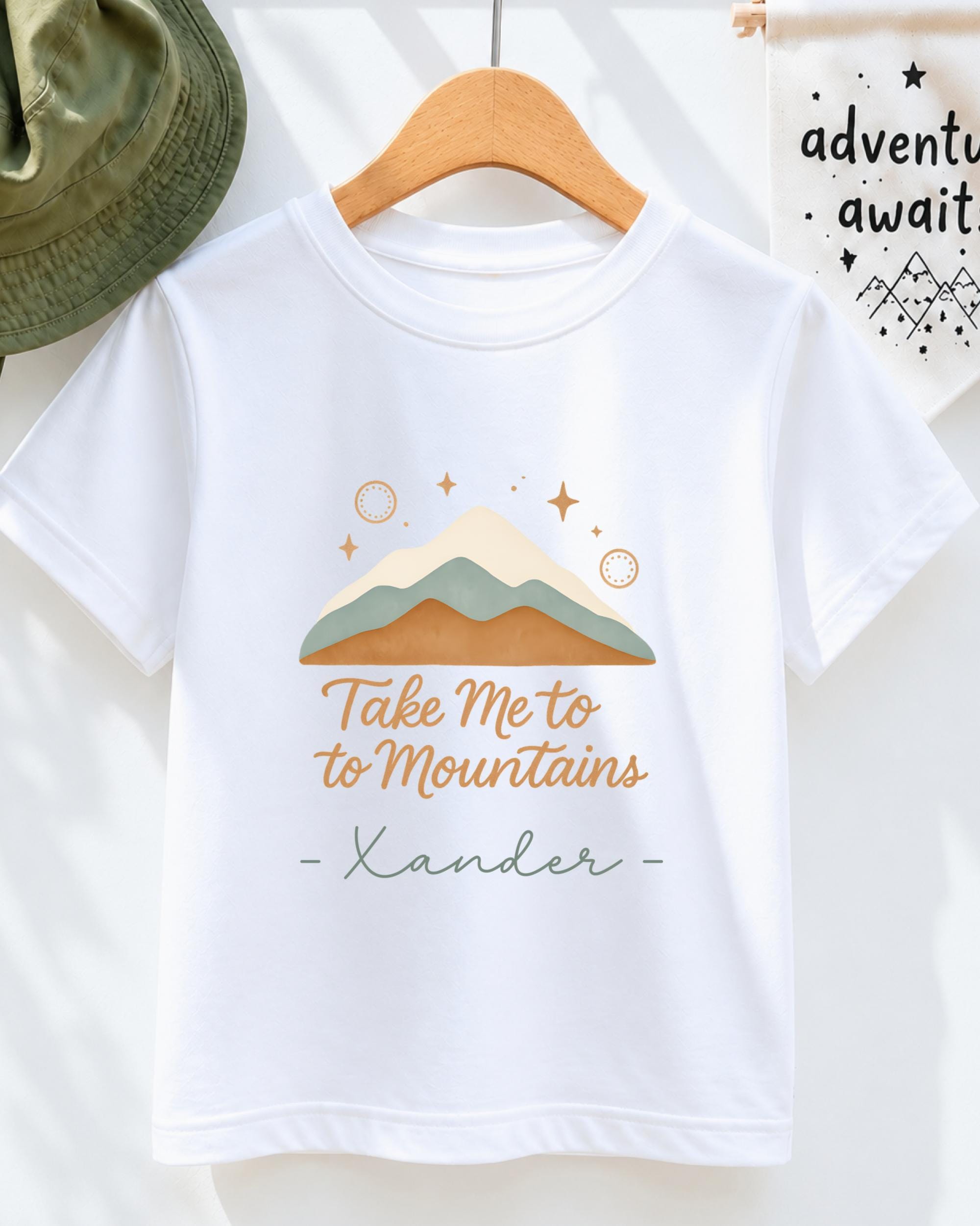 A white t-shirt with a mountain and starry sky design, along with the text "Take Me to to Mountains" and the name "Xander" printed on it.