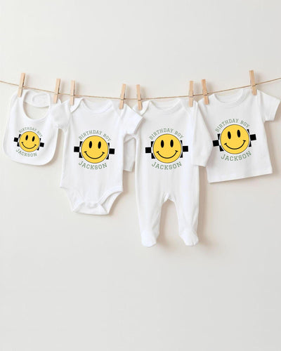 A collection of white baby clothes with yellow smiley faces printed on them, hanging on a clothesline.