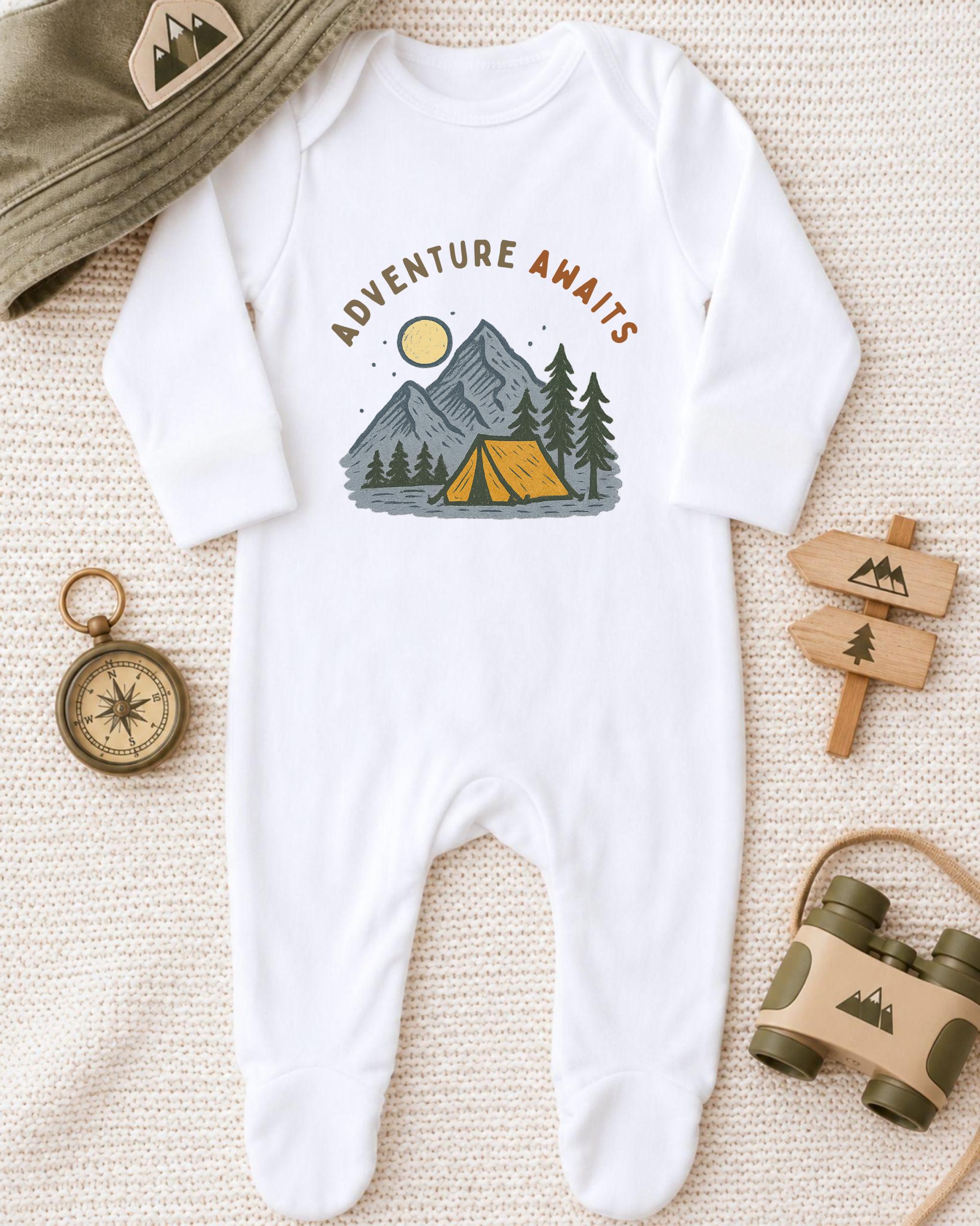 A baby onesie with a camping scene printed on it, along with camping gear such as a compass, binoculars, and a hat.
