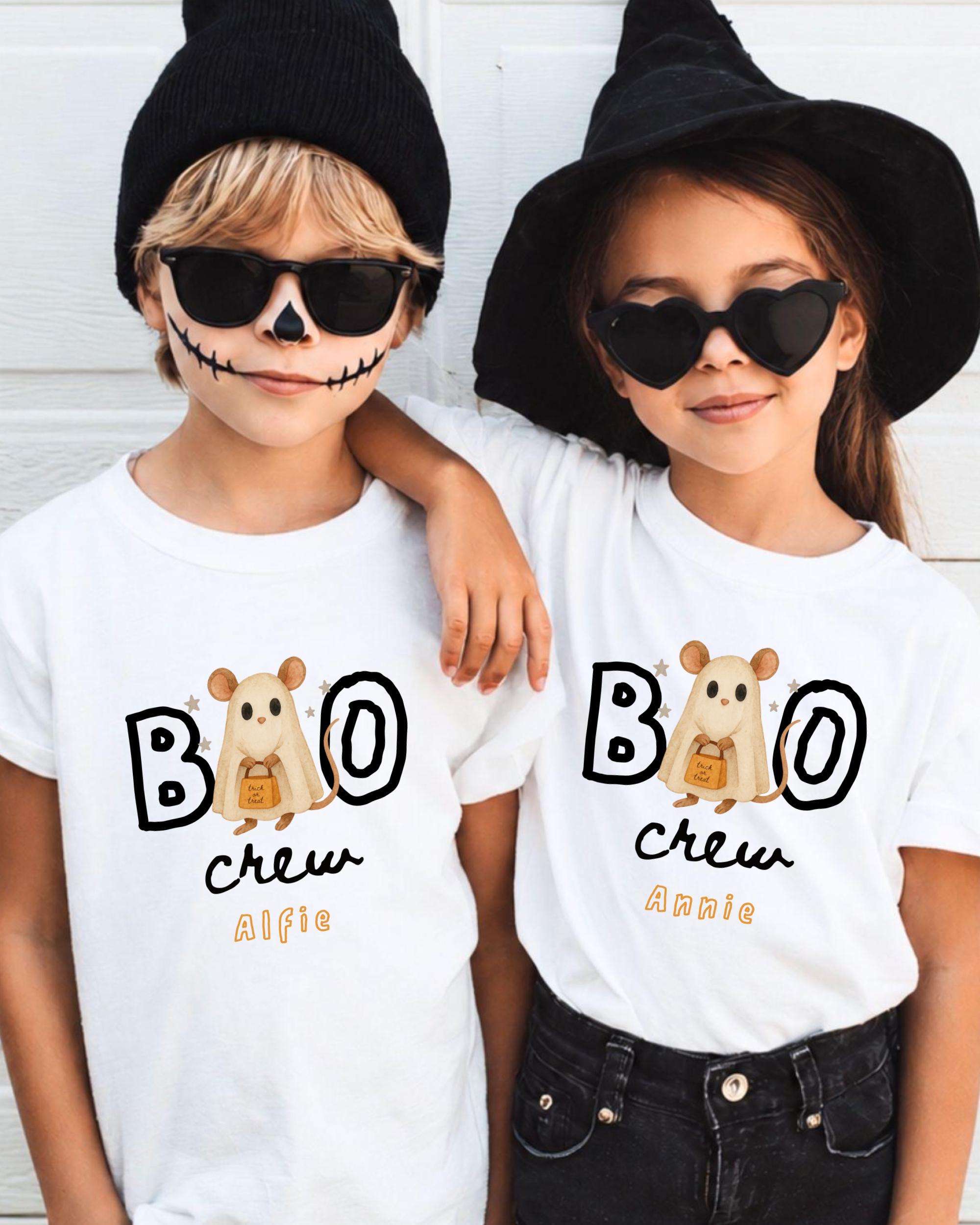 Two children wearing white t-shirts with the text "BOO" and "CREW" printed on them, along with a cartoon character, are posing together.