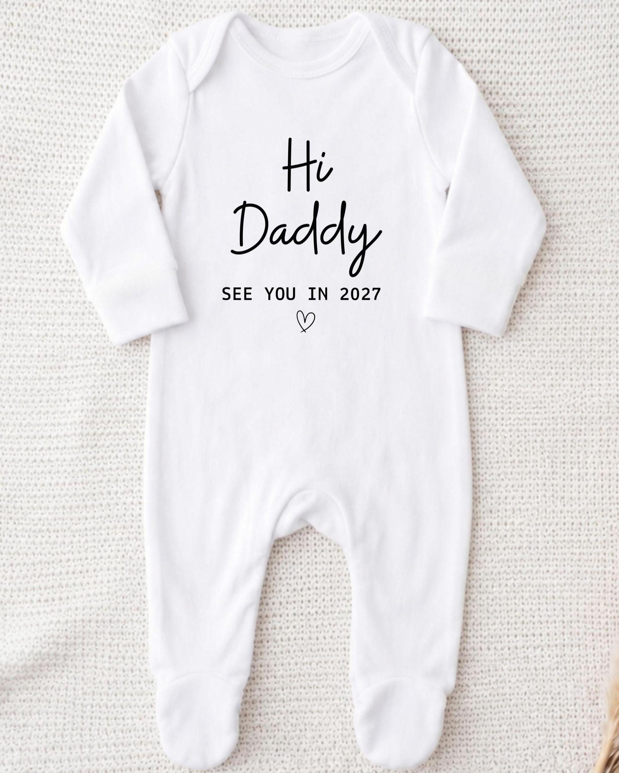 A white onesie with the text "Hi Daddy See You in 2027" printed on it.
