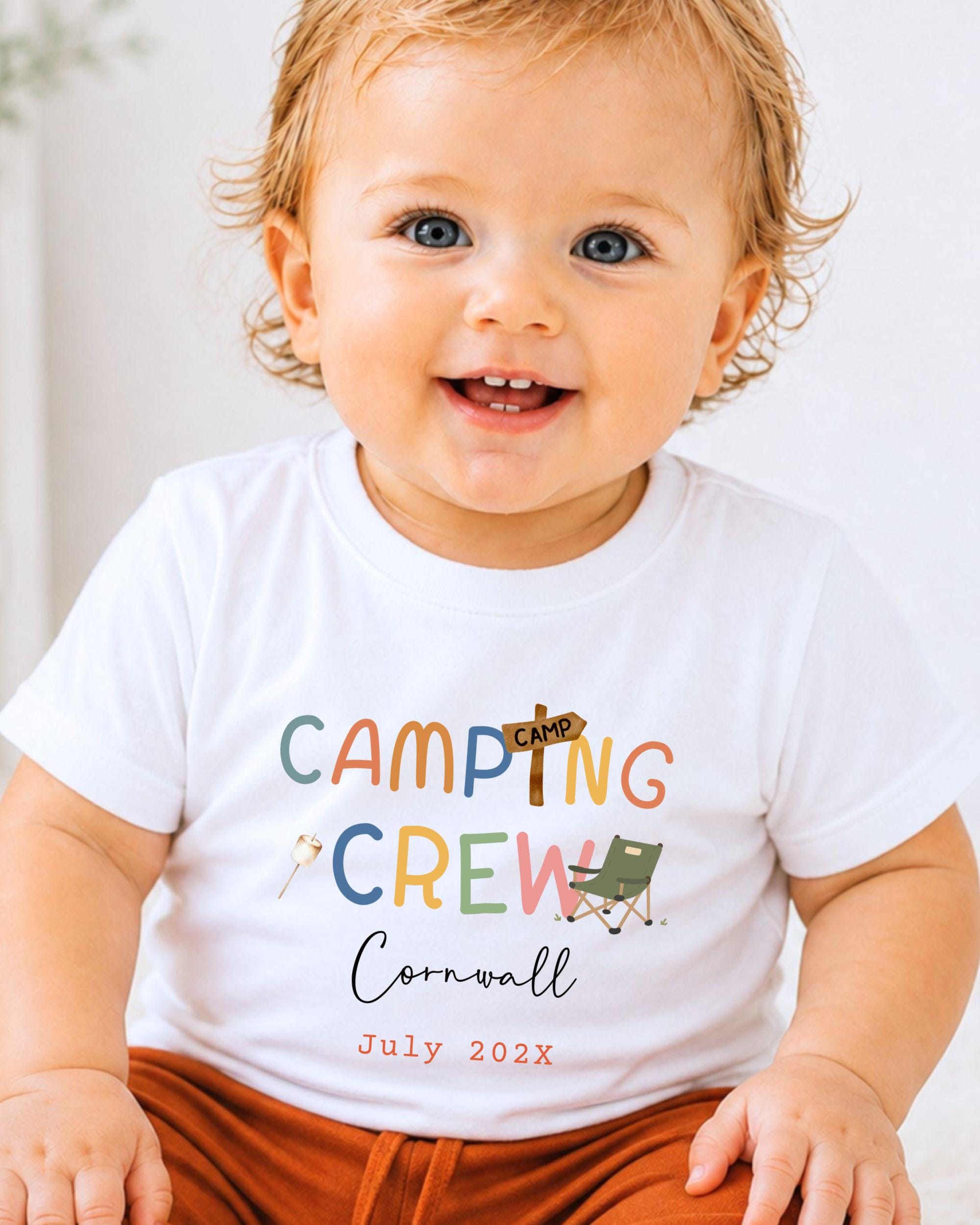A smiling baby wearing a white t-shirt with the text "CAMPING CREW Cornwall July 2023" printed on it.