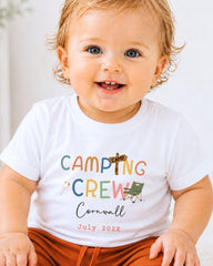 A smiling baby wearing a white t-shirt with the text "CAMPING CREW Cornwall July 2023" printed on it.