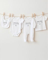 A collection of white baby clothes, including onesies and pajamas, hanging on a clothesline.