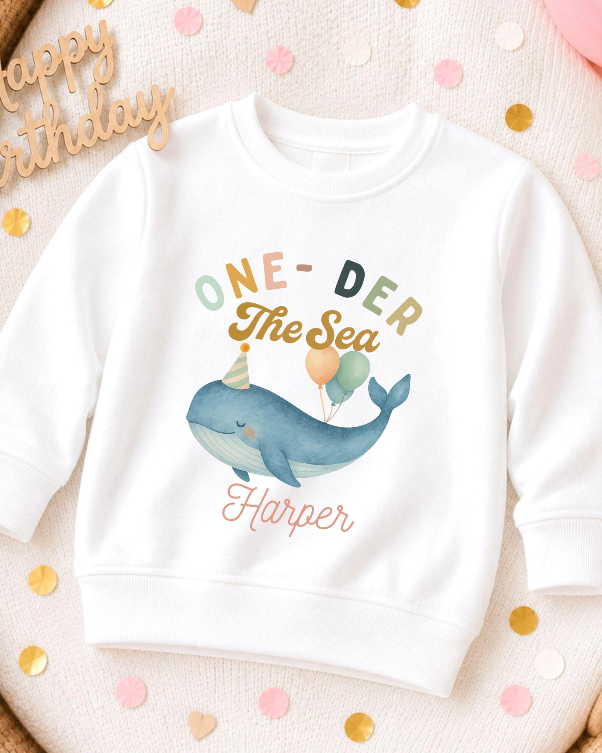 A white sweatshirt with a colorful graphic of a whale and balloons, along with the text "One-DER The Sea Harper" printed on it.