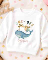 A white sweatshirt with a colorful graphic of a whale and balloons, along with the text "One-DER The Sea Harper" printed on it.
