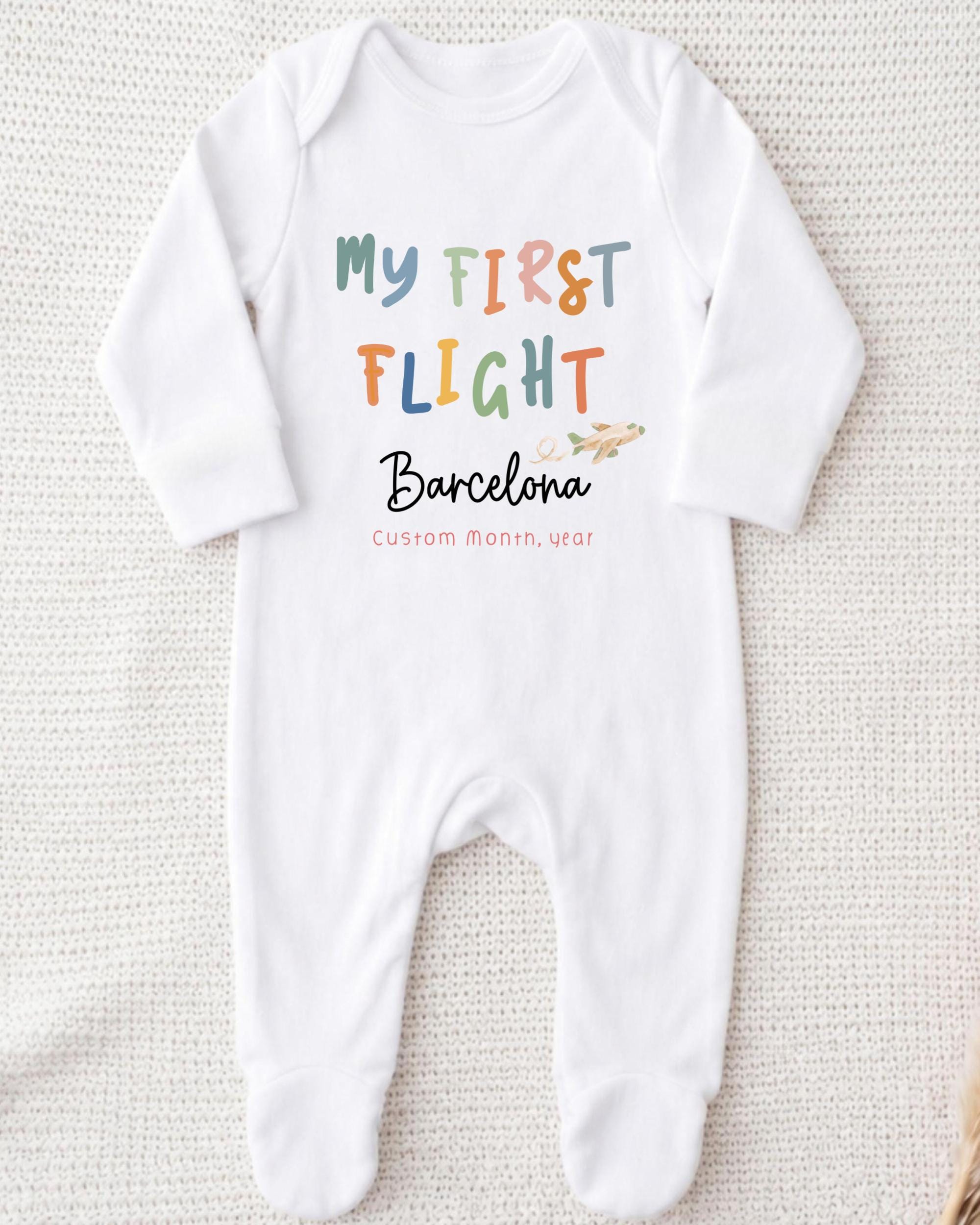 A white onesie with the text "My first flight Barcelona Custom month/year" printed on it.