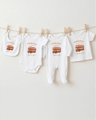 A row of white baby clothes with a red double-decker bus printed on them, hanging on a clothesline.
