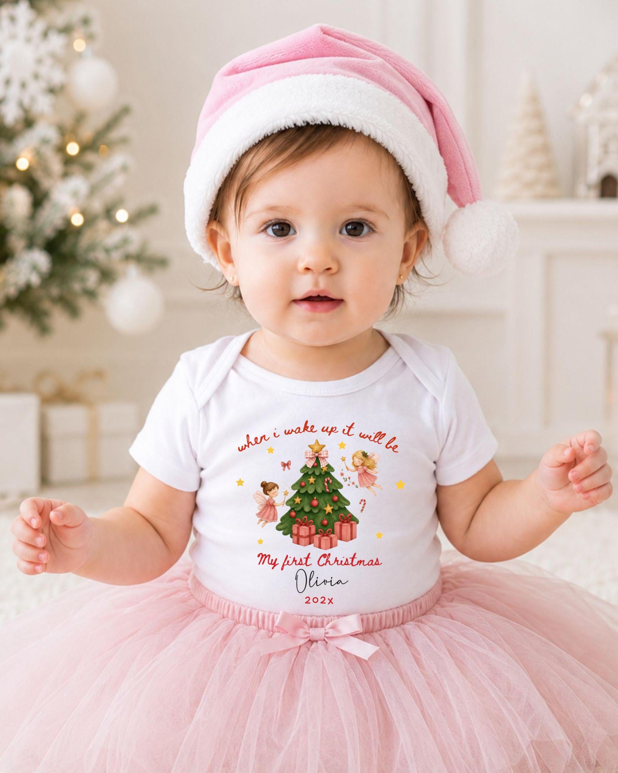 A young girl wearing a pink hat and a white t-shirt with a Christmas tree design, posing in front of a Christmas tree.