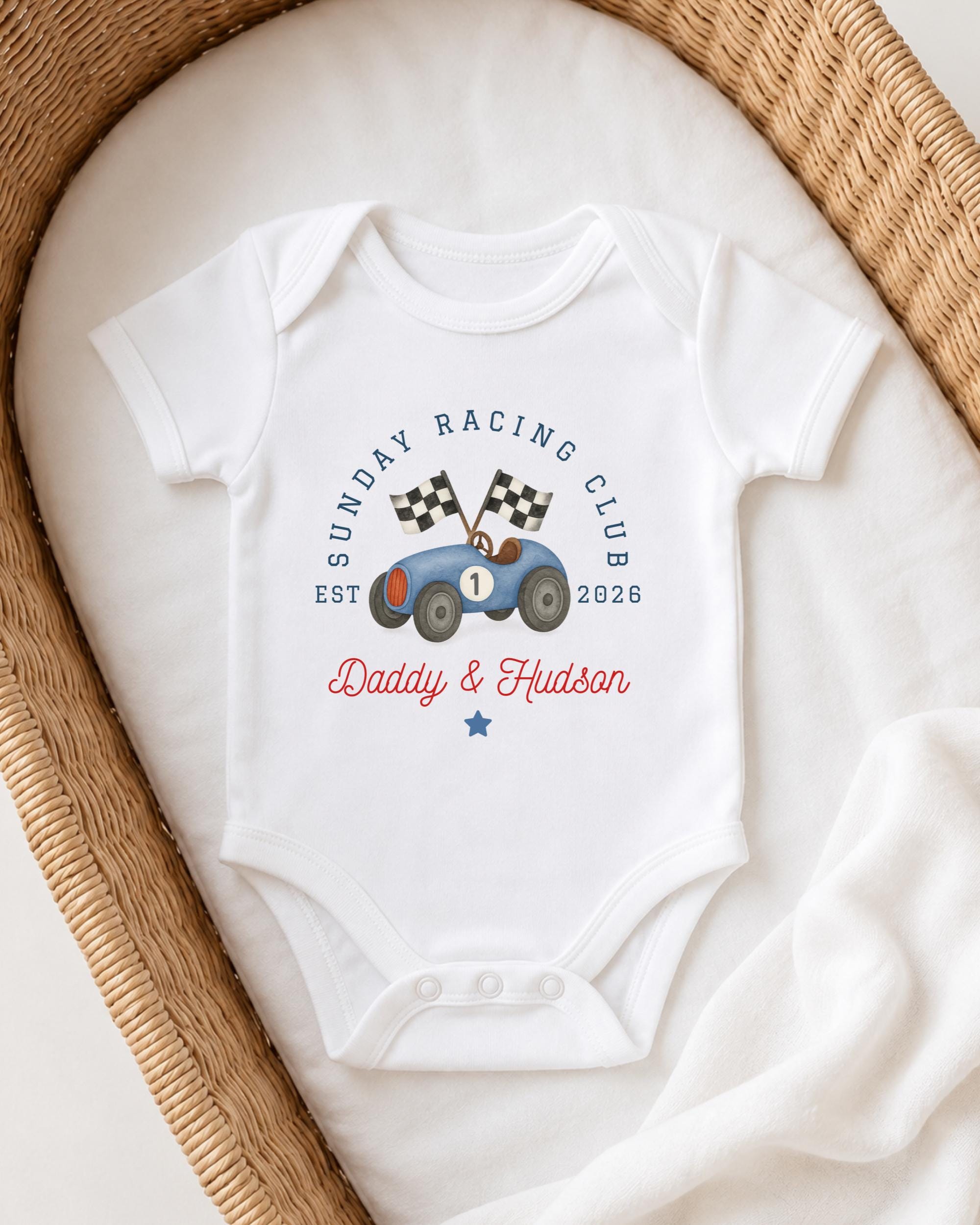 A white onesie with a graphic of a race car and the text "Sunday Racing Club" printed on it, placed in a woven basket.