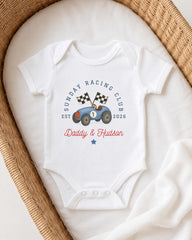 A white onesie with a graphic of a race car and the text "Sunday Racing Club" printed on it, placed in a woven basket.