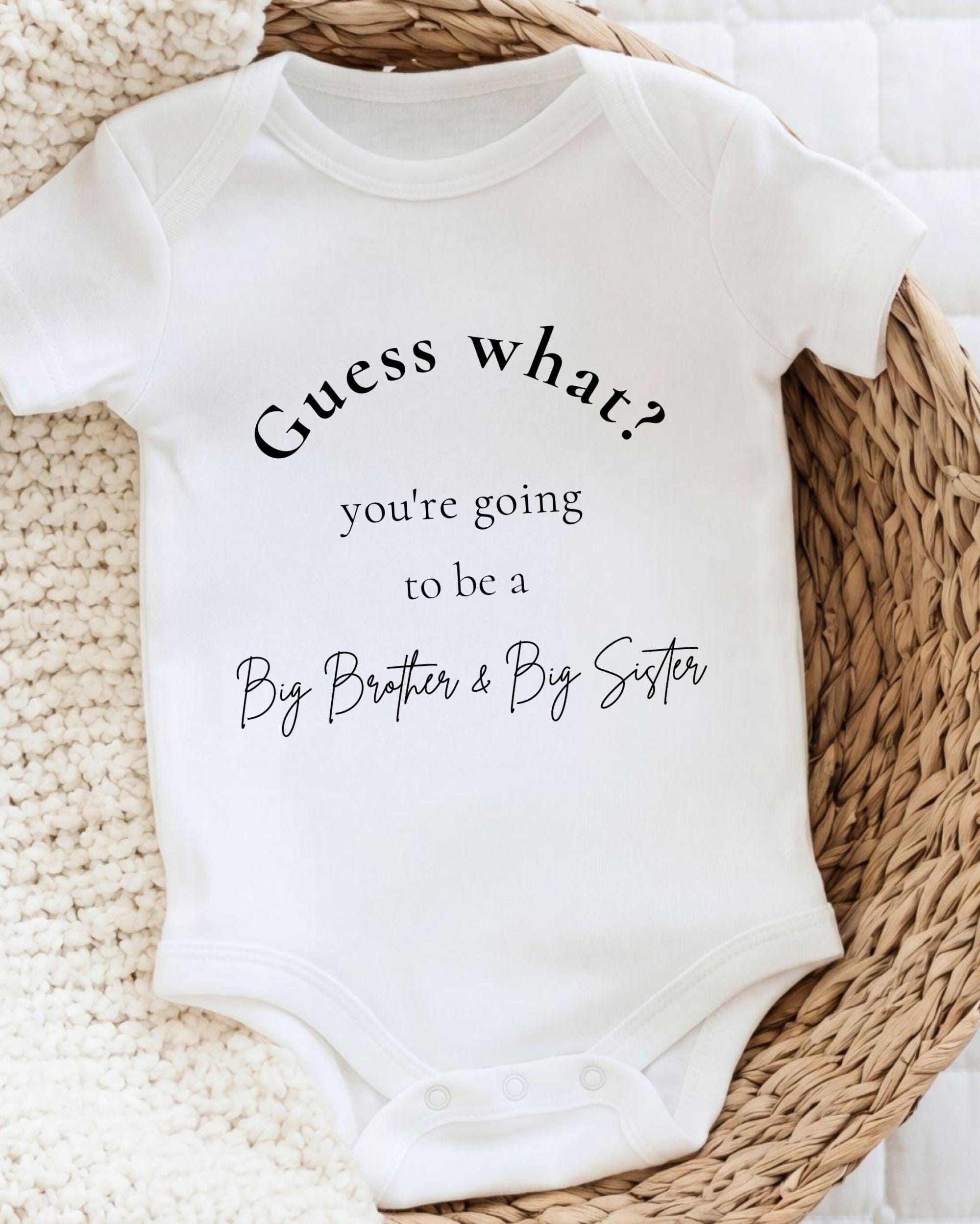 A white baby onesie with text that says "Guess what? you're going to be a Big Brother & Big Sister" printed on it.