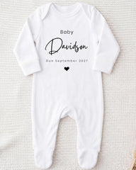 A white onesie with the text "Baby Davidson Due September 2027" printed on it.