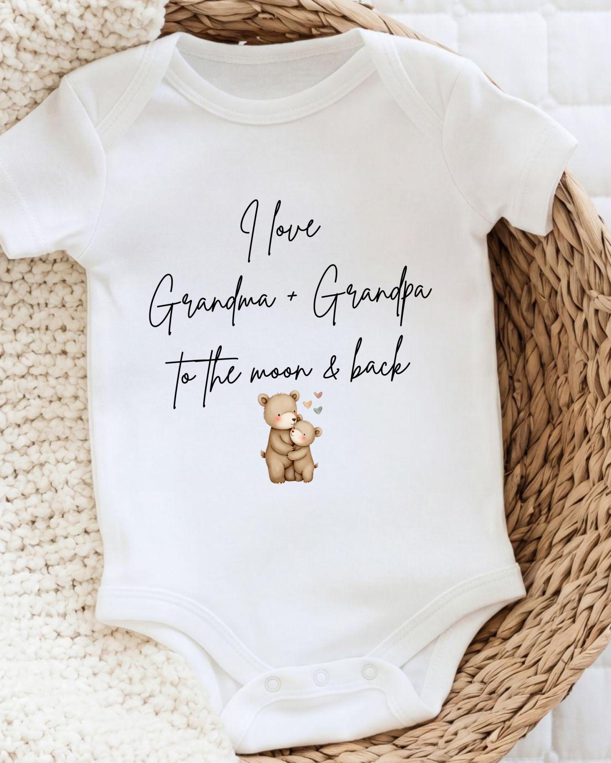 A white baby onesie with a printed message that reads "I love Grandma + Grandpa to the moon & back".