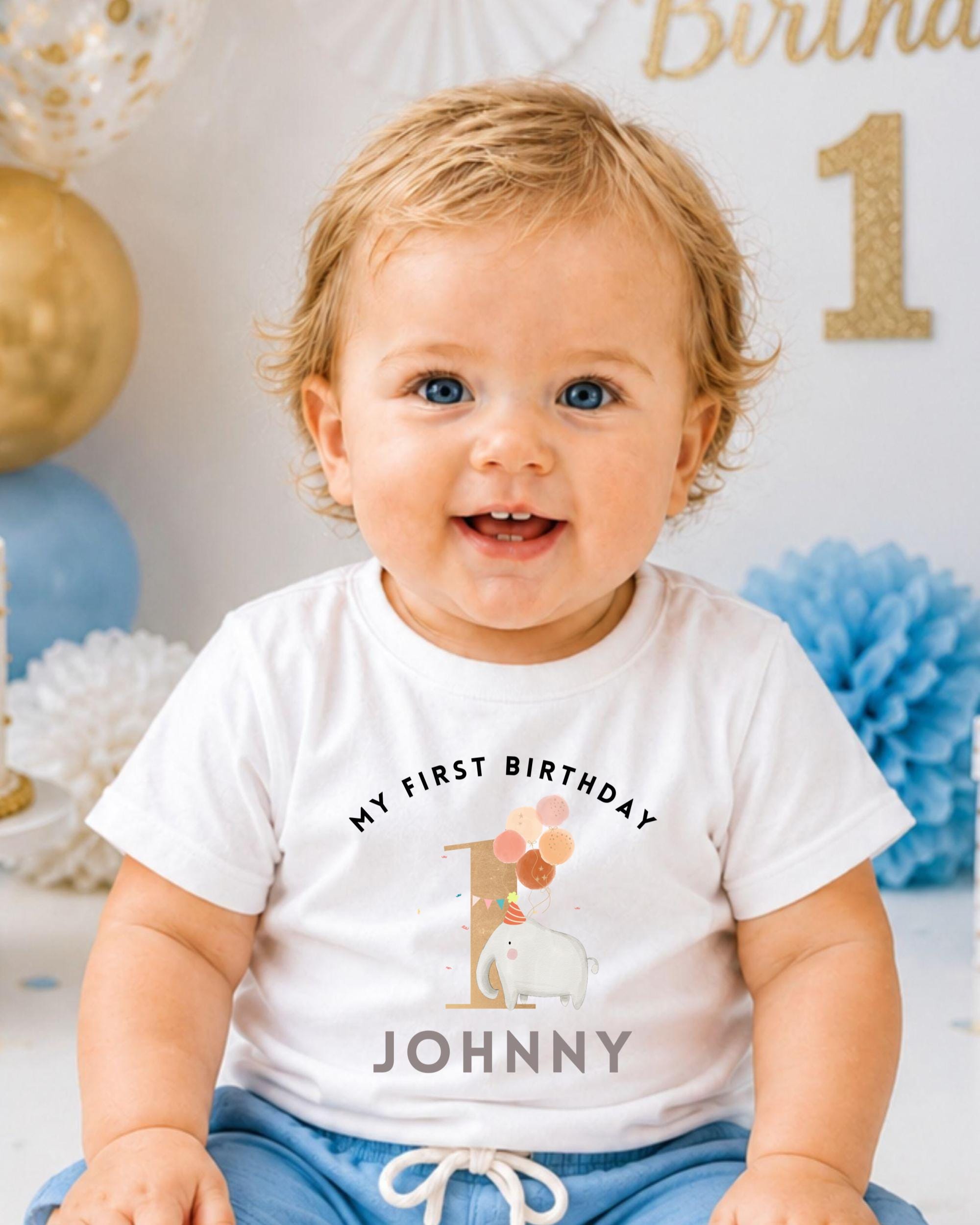 A smiling baby boy wearing a white t-shirt with a birthday message and an elephant graphic.