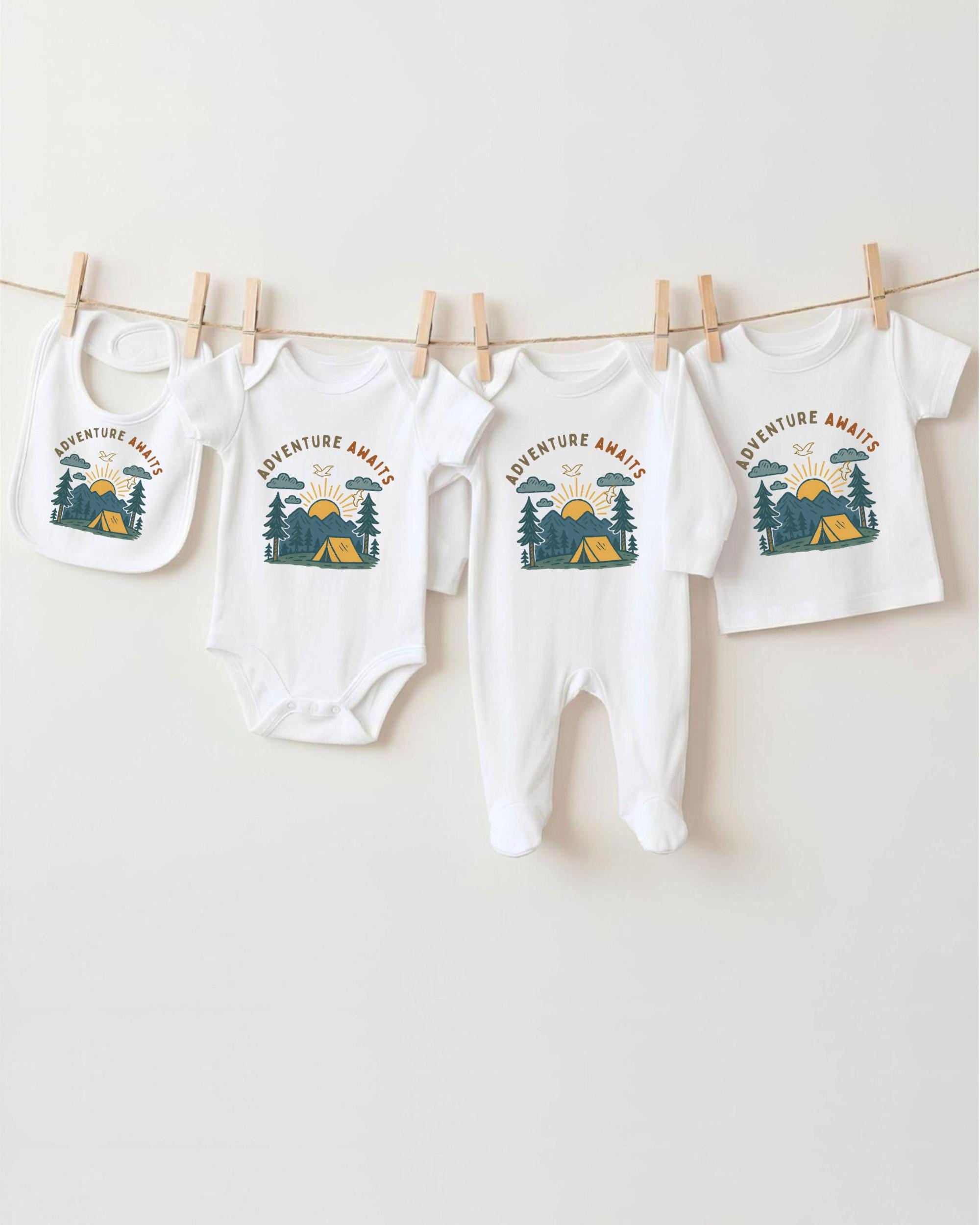 A collection of baby clothes, including onesies and bibs, hanging on a clothesline with camping-themed designs.