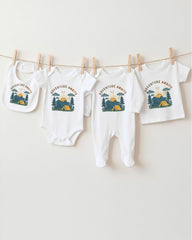 A collection of baby clothes, including onesies and bibs, hanging on a clothesline with camping-themed designs.