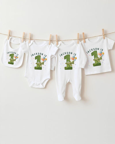 A collection of white baby clothes, including bodysuits and bibs, with the text "JACKSON IS" printed on them. The clothes are hanging on a clothesline, with the first and third items being the largest.