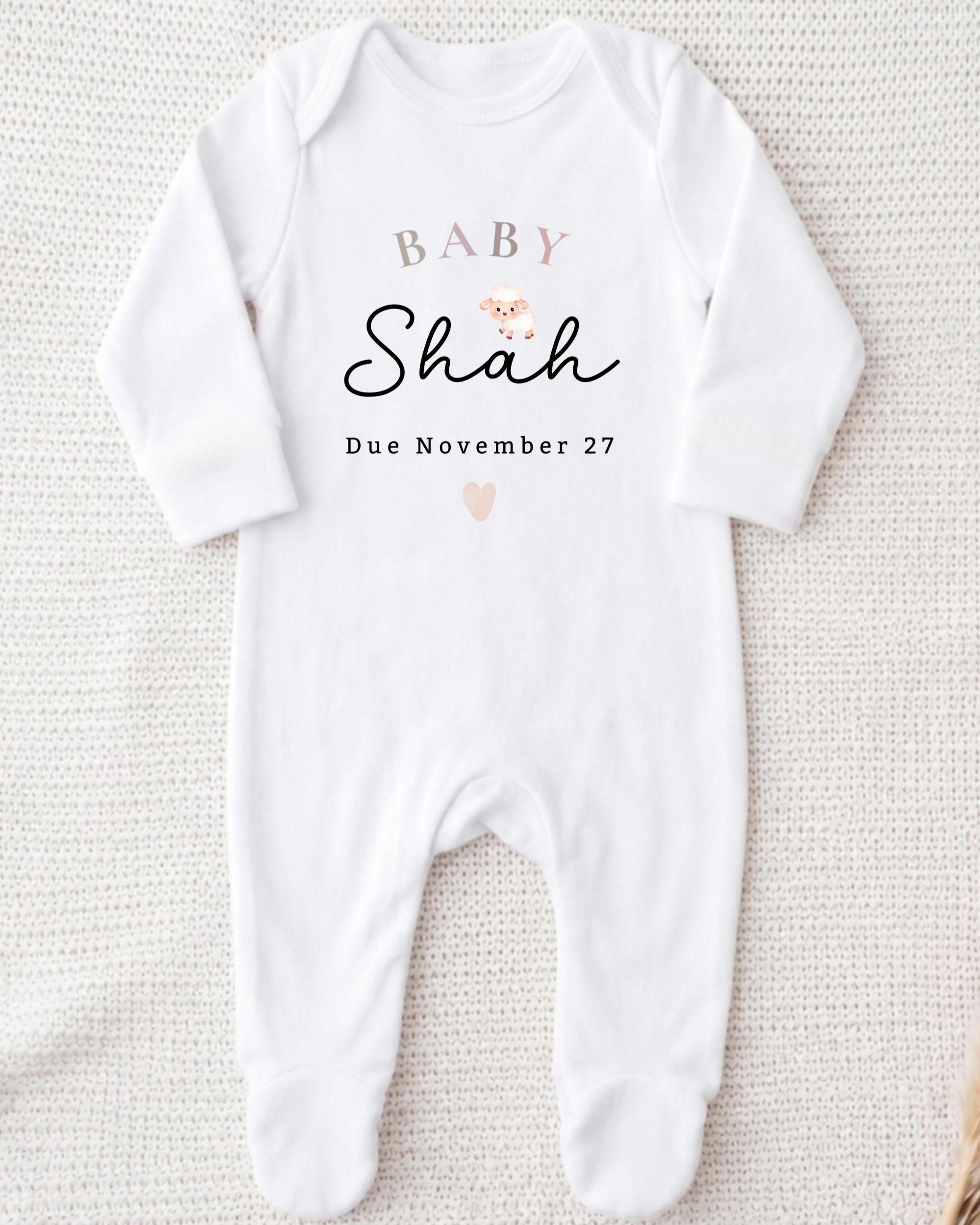 A white onesie with text and a heart graphic, indicating the name and due date of a baby named Shah.