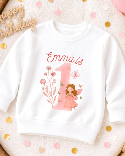 A white sweatshirt with a pink fairy and the number 1 printed on it, surrounded by confetti.