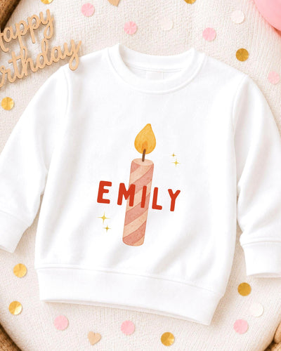 A white sweatshirt with a personalized name printed on it, along with a candle design.